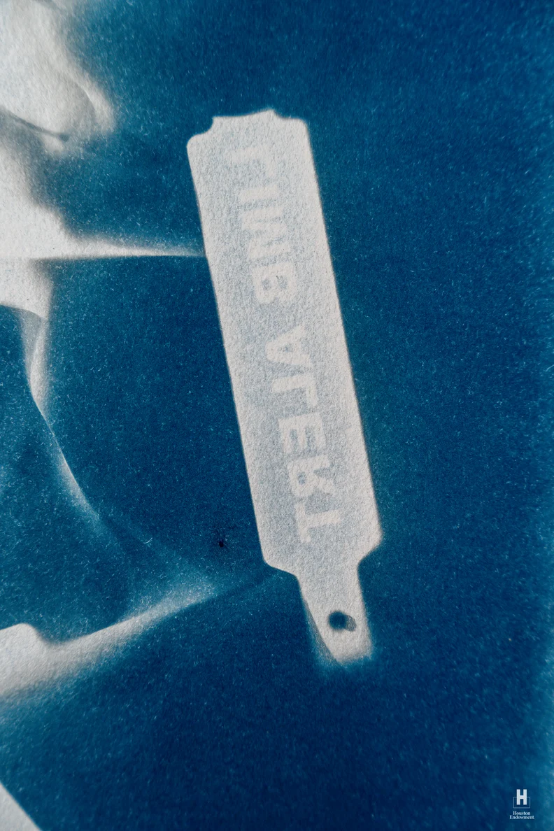 White rectangular luggage tag with a small punched hole and faint, reversed printed letters, set against a textured deep cyan background.