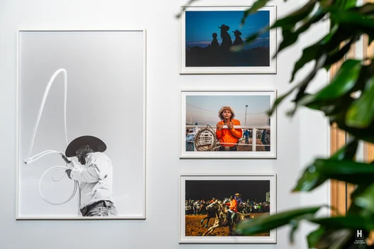 Gallery wall: large B&W cowboy spinning a lasso, color rodeo photos including a young cowboy in orange and bronc action, leaves at right.