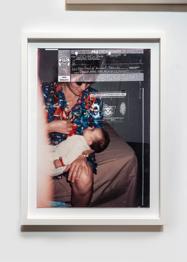 Framed photo of a woman in a floral blouse holding a sleeping infant on her lap, overlaid with photocopied ID documents and a check.